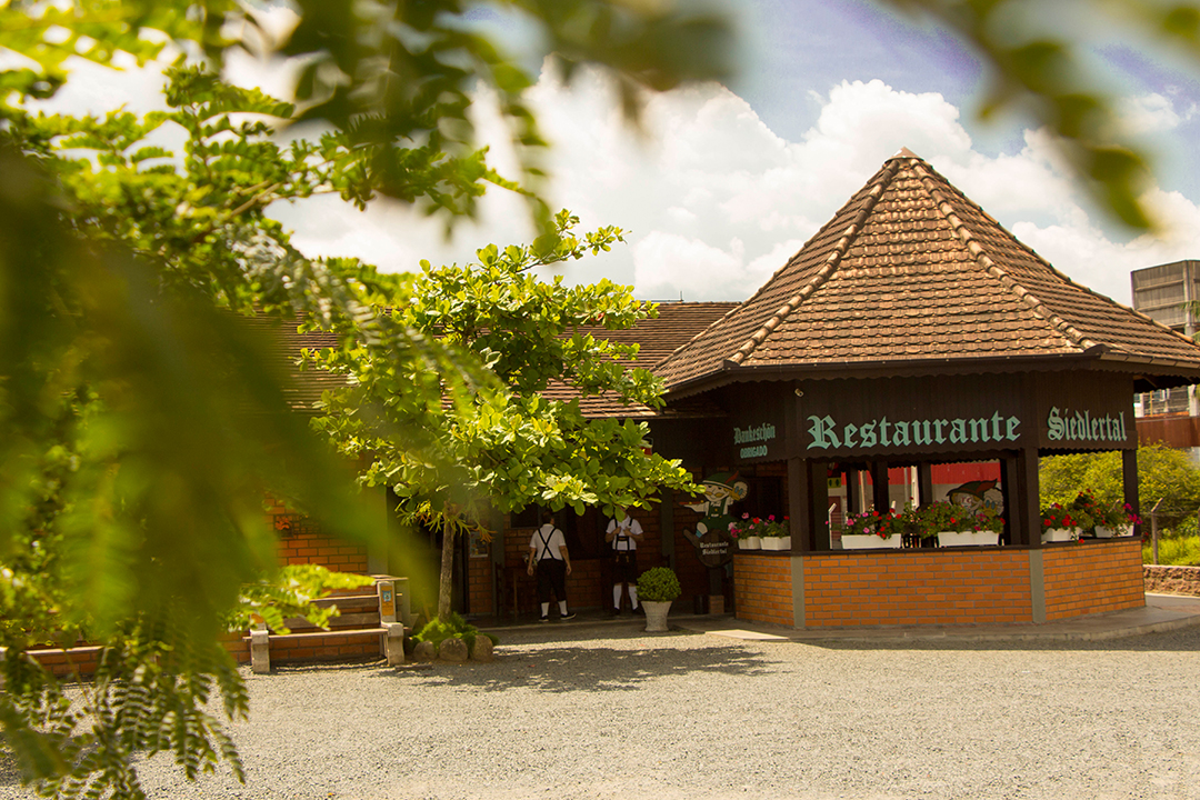 Entrada do restaurante vista entre as árvores, com equipe em traje típico